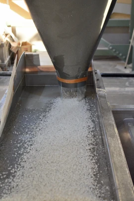 A machine processing plastic pellets through a funnel and onto a tray in a factory setting.