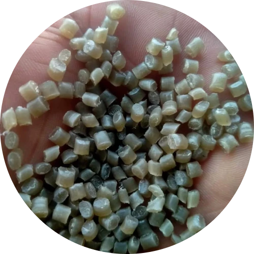 A close-up of a hand holding light brown and gray plastic pellets, showcasing processed recycled materials.