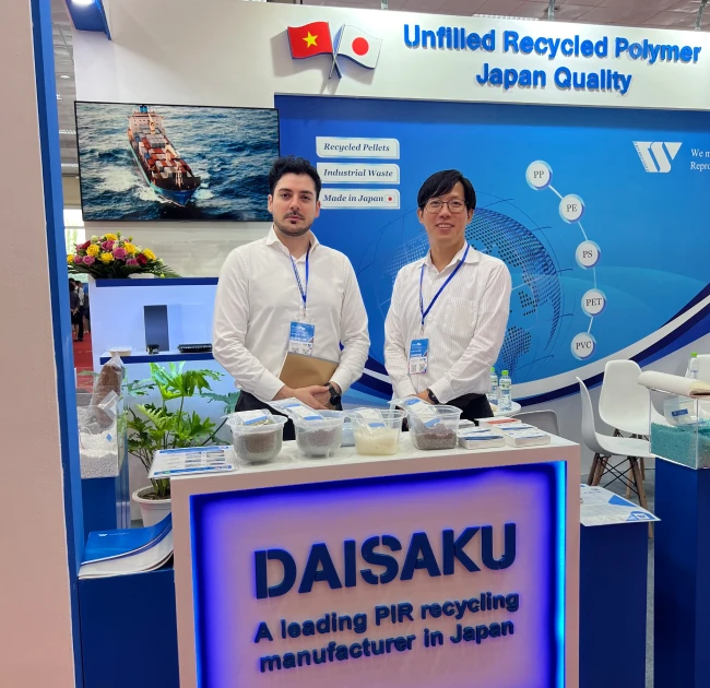 Two representatives from DAISAKU CO., LTD. standing at a booth promoting unfilled recycled polymer products from Japan at an industry trade show in Vietnam.