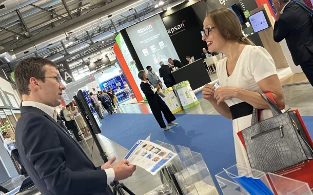 A business professional from Daisaku on the left engaging in a convesation with a woman at a trade show, discussing about Daisaku materials, set in a large exhibition hall.