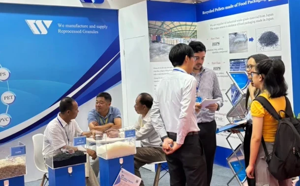 A group of professional at a trade show booth for DAISAKU, discussing reprocessed granules and recycled materials, with displays of plastic pellets and detailed informational banners in the background.
