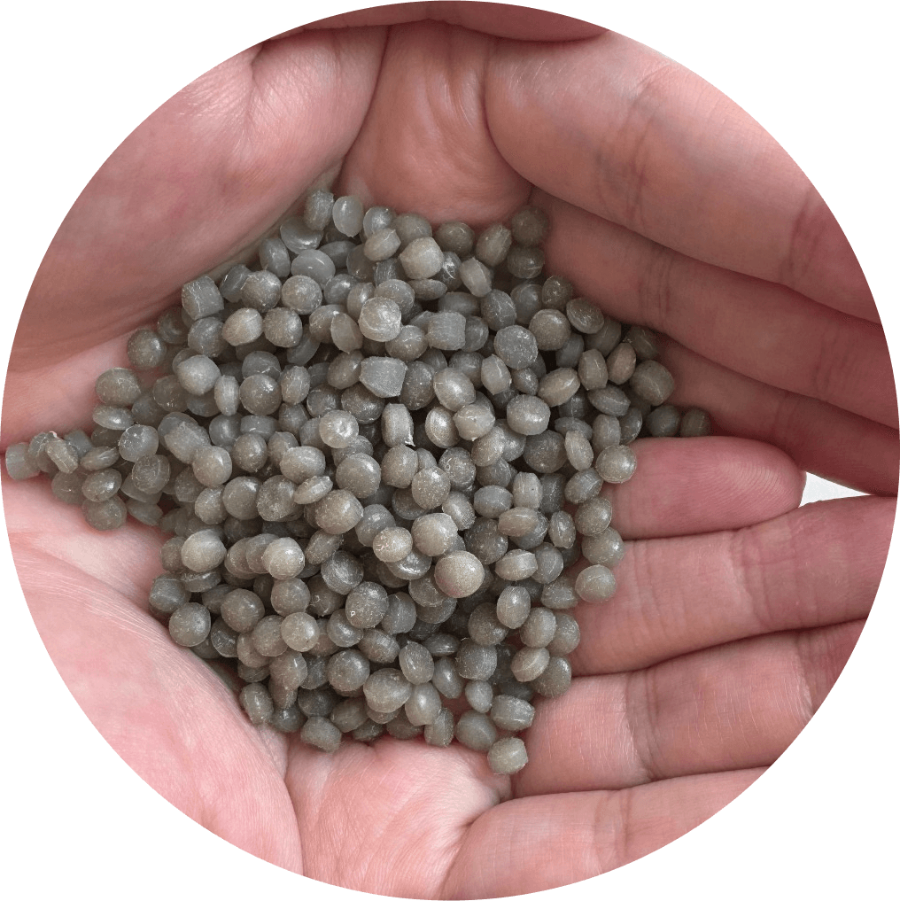 A close-up of a hand holding light brown and gray plastic pellets, showcasing processed recycled materials.
