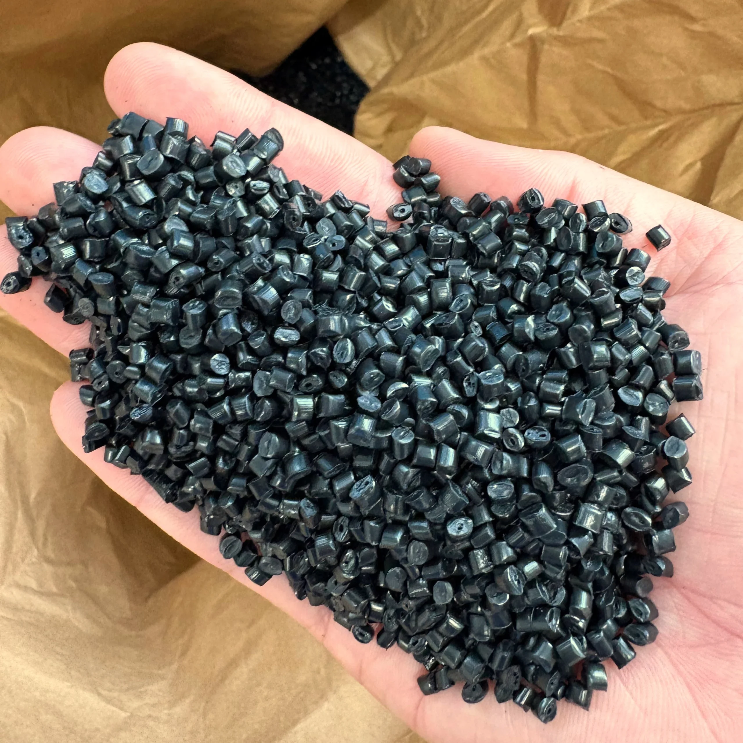 A person holding a large amount of small black plastic pellets in their hand, emphasizing the high-quality raw materials used in production.